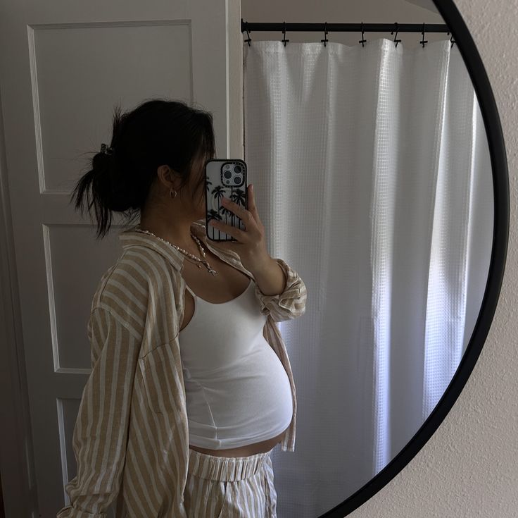 a pregnant woman taking a selfie in front of a mirror with her cell phone