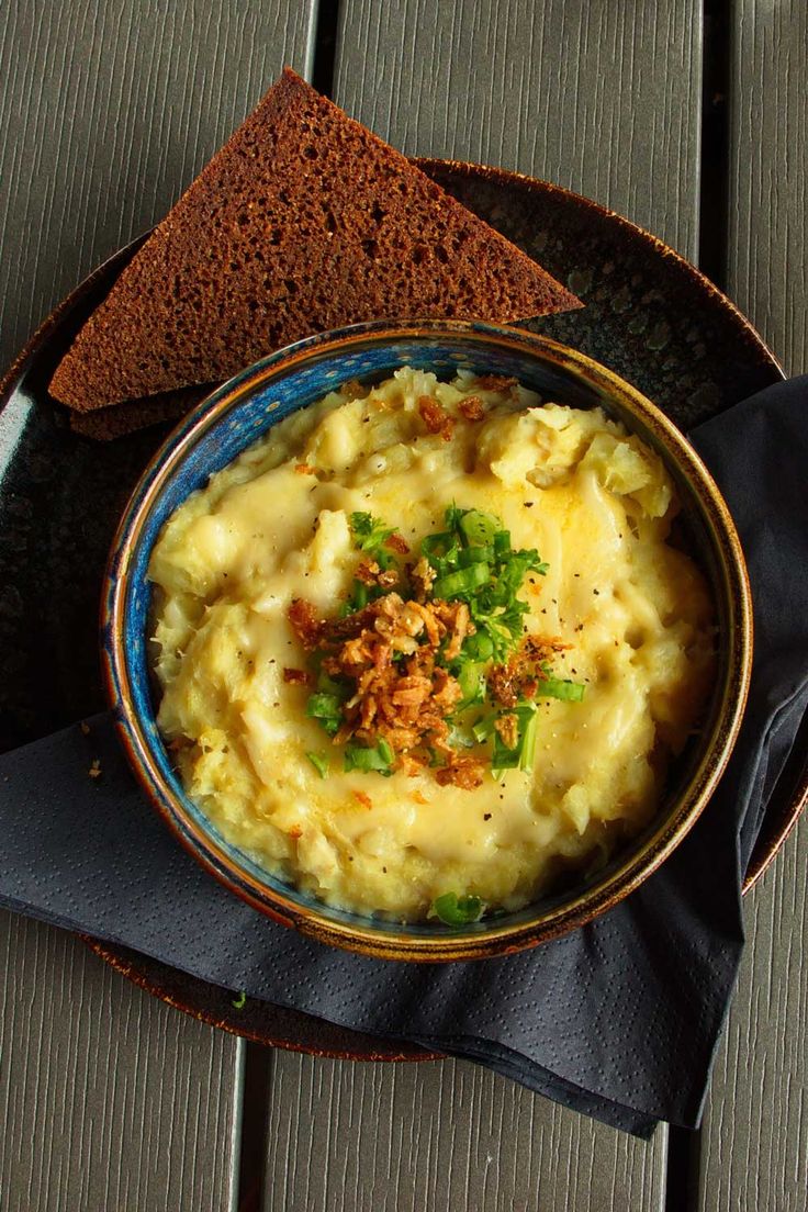 a bowl of mashed potatoes and bread on a wooden table with a blue napkin