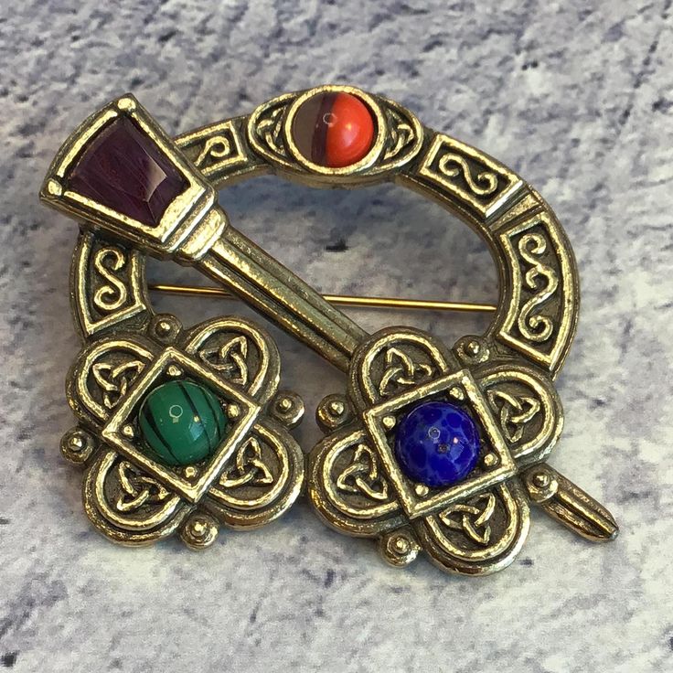 Lovely vintage brass-tone signed Miracle Celtic-style penannular brooch with Tara sword and faux agate stones. Rollover clasp closure. It measures 2 and 1/8 inches x 1 and 3/4 inches In good vintage condition. The pin and clasp secure. Penannular Brooch, Celtic Style, Agate Stone, Vintage Brass, Halloween Shopping, Brooch Pin, Brooches, Agate, Accessory Gift