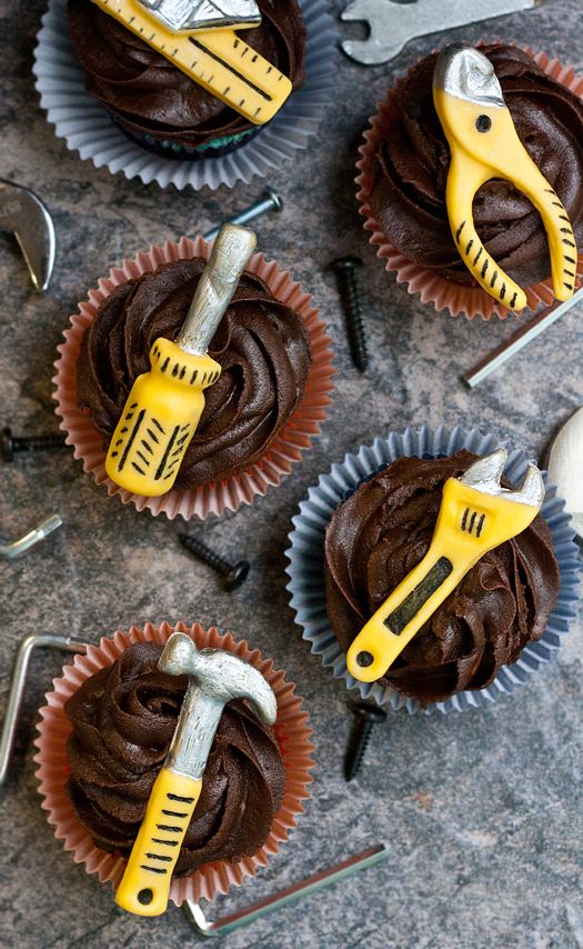 four cupcakes with chocolate frosting and construction tools on the top one is yellow