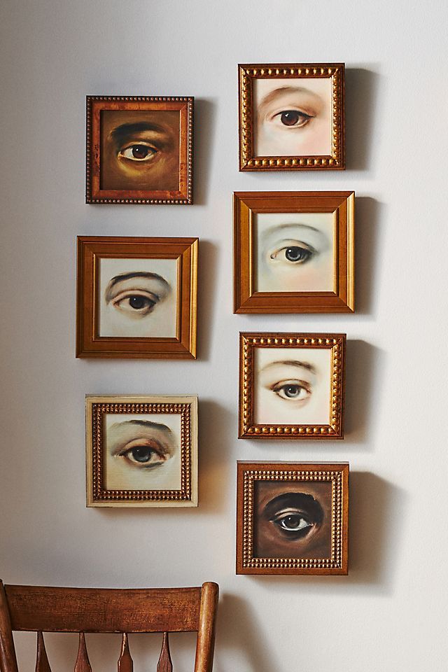 several framed pictures hang on the wall next to a wooden chair with an eyeball painted on it