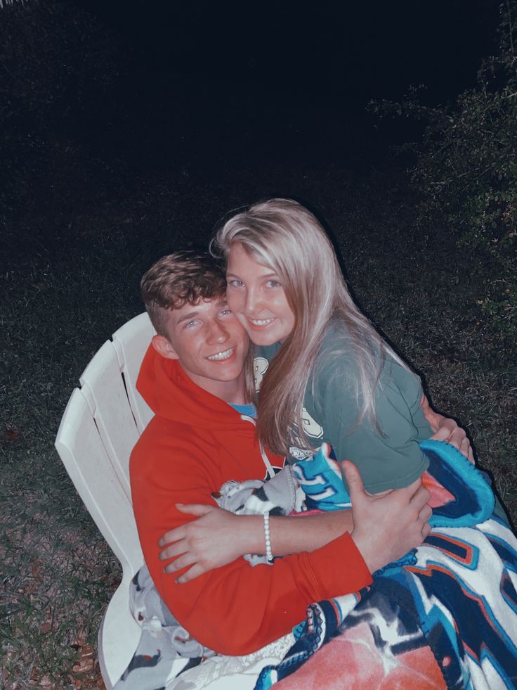 a man and woman hugging each other on a lawn chair in the grass at night