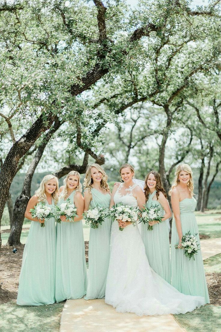 a bride and her bridesmaids pose for a photo under the trees at their wedding