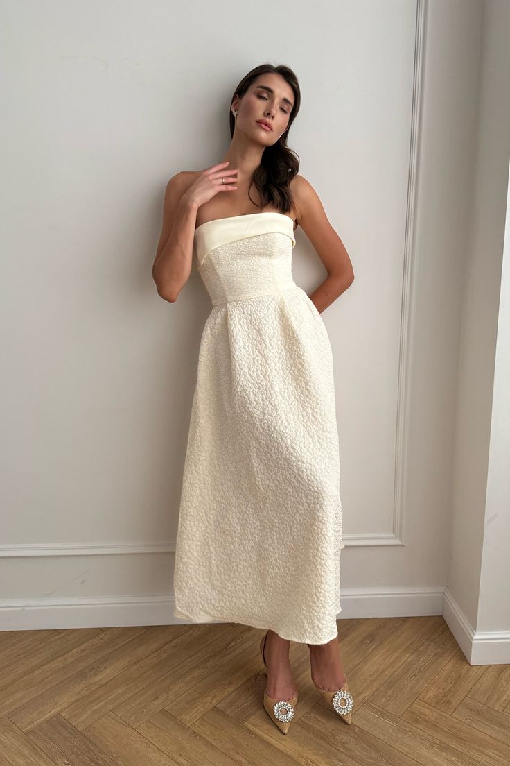 a woman in a white dress leaning against a wall