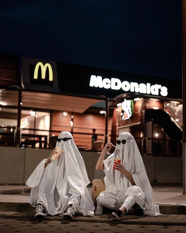 two people dressed in white sitting on the ground next to mcdonald's at night