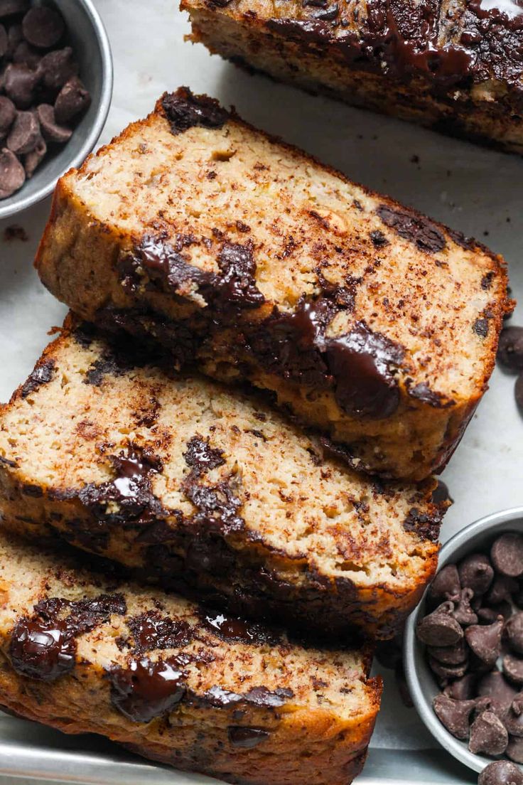 slices of chocolate chip banana bread on a plate with bowls of chocolate chips around them