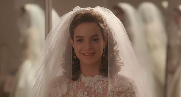 a woman wearing a wedding dress and veil in front of a mirror with dresses behind her