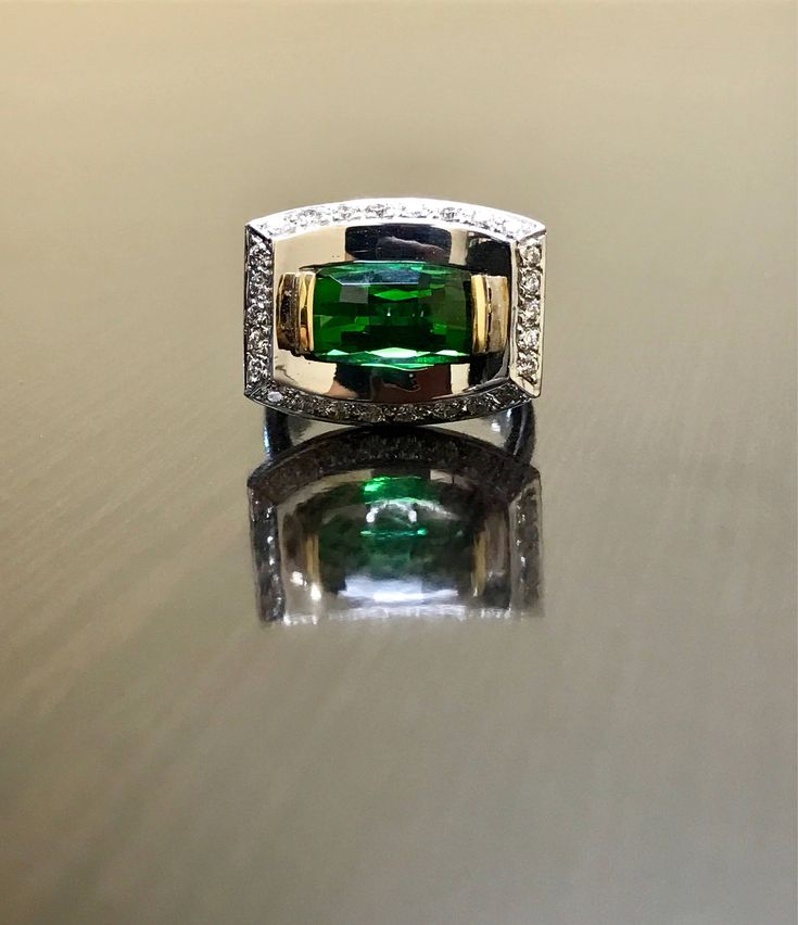 an emerald and diamond ring sitting on top of a table