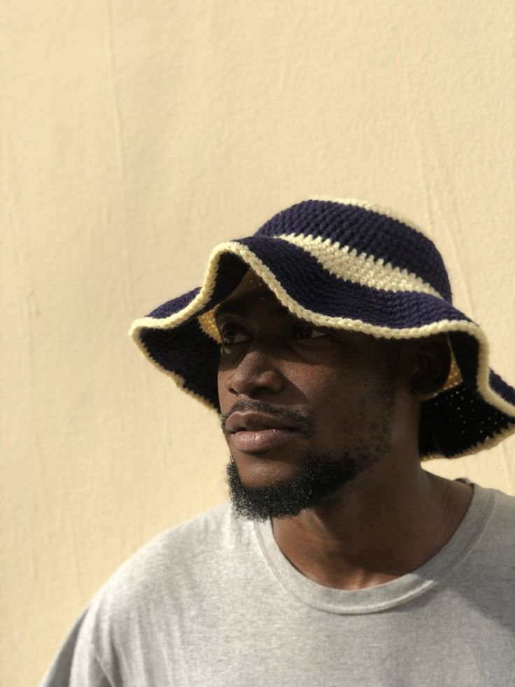 a man wearing a blue and white hat with stripes on the brim, standing in front of a yellow wall