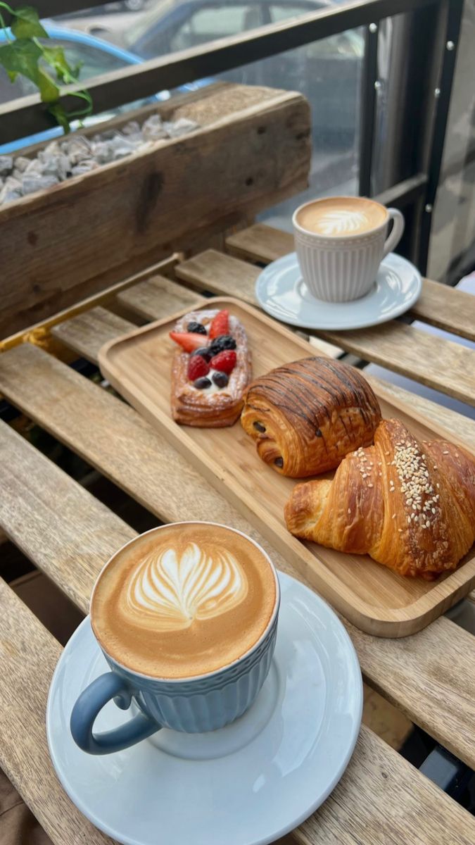 two croissants and a cup of coffee sit on a wooden table outside