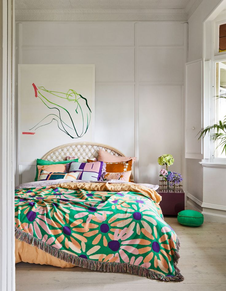 a bed with colorful comforters and pillows in a white room next to a window