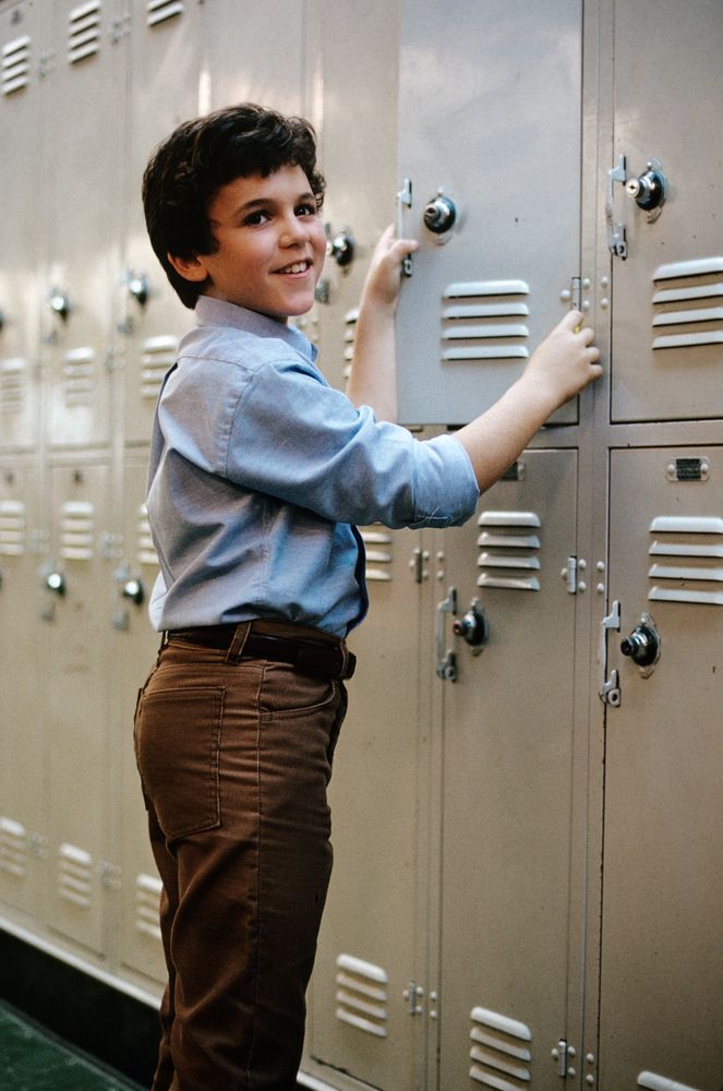 a young boy is leaning against a locker