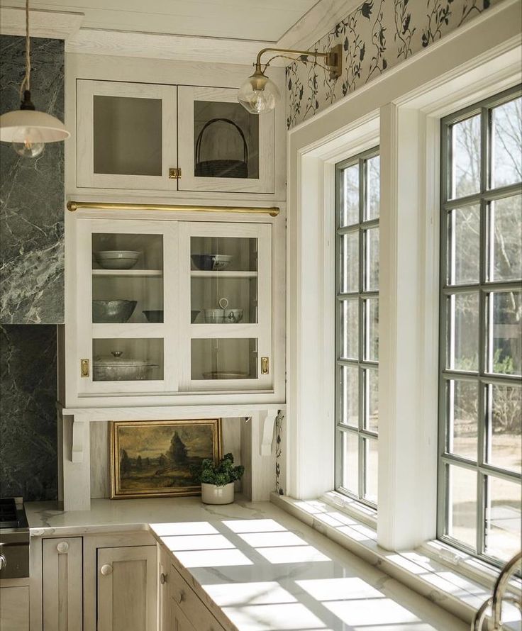 a kitchen with white cabinets and marble counter tops, along with an open window to the outside