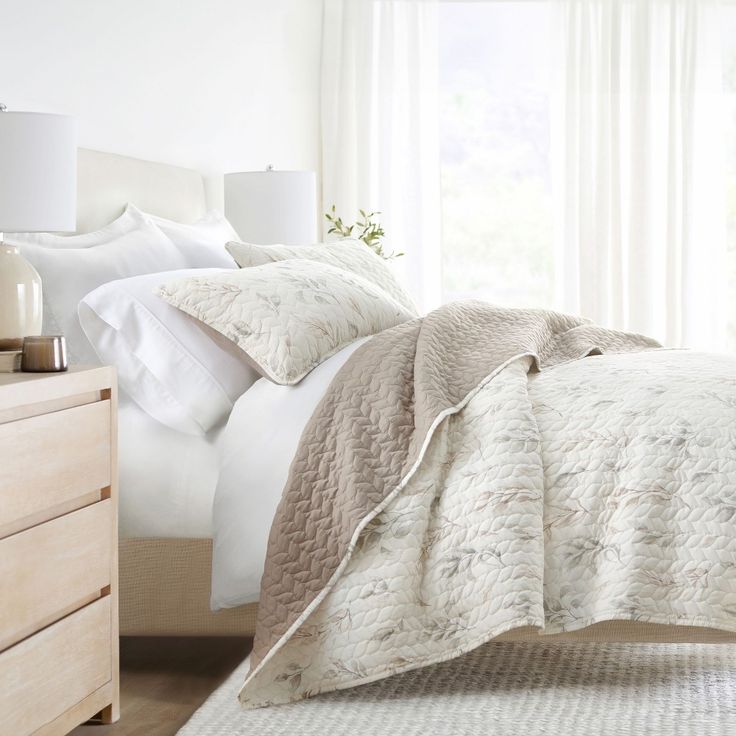 a bed with white comforter and pillows in a bedroom next to a window,