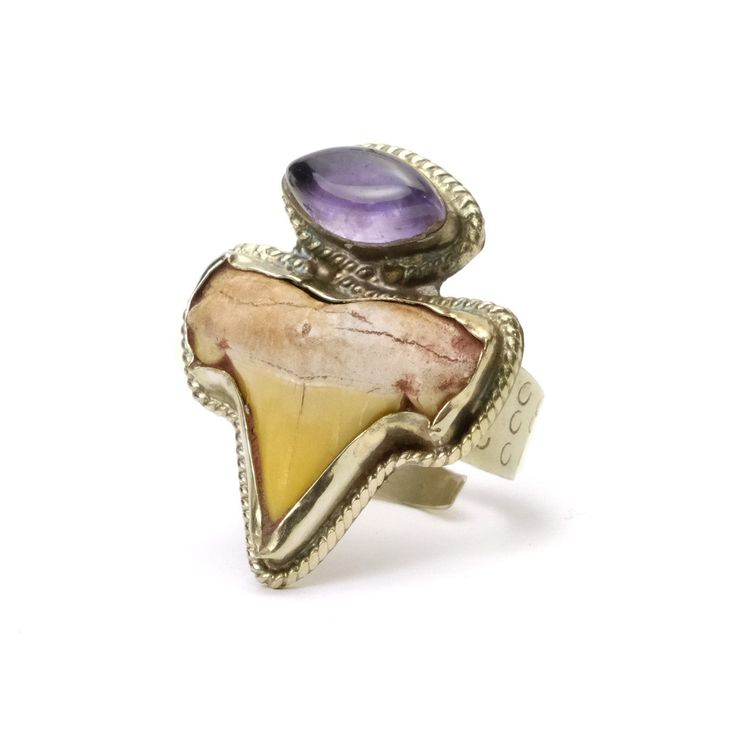 Shark Tooth Ring with Amethyst Cabochon Ring size: 6-11 adjustable Top measurements: 1.2"L x 0.9"W x 0.3"T Materials: Hand Stamped White Brass with an Hand Inset Shark Tooth and Amethyst Cabochon Hand Crafted in Nepal Adjustable Round Multi-stone Jewelry, Heirloom Nickel-free Jewelry For Collectibles, Collectible Spiritual Jewelry Ring, Heirloom Nickel-free Collectible Jewelry, Spiritual Collectible Jewelry Rings, Artisan Multi-stone Adjustable Jewelry, Oval Amethyst Jewelry Collectible, Adjustable Nickel-free Open Ring Jewelry, Artisan Adjustable Multi-stone Jewelry