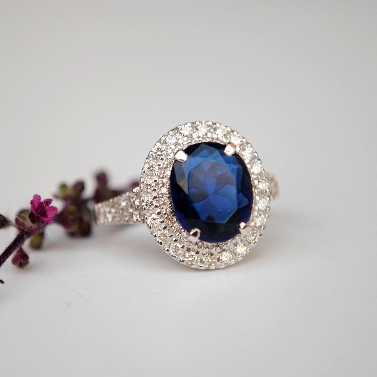 "A ring style of the royalties, this design flaunts an oval synthetic blue stone, surrounded by 0.66cts of double natural diamond halo. Crafted in solid 14k gold, the shank tapers and has diamonds enhancing the overall look. * Center Stone : Blue Sapphire Imitation (for natural, please message) * Shape : Oval (10x8 mm) * Halo Gemstones : Natural Genuine Diamonds * Diamond Wt. : 0.66 Cts * Color/Clarity : H-I, Vs-Si * Gold - 14kt, 5.9 gms solid white gold (approx) If you like this ring, please pr Luxury Sapphire Oval Halo Ring, Luxury Oval Cluster Ring With Halo Setting, Luxury Blue Oval Cluster Ring, Luxury Oval Sapphire Halo Ring, Oval Diamond Cluster Ring With Halo Setting, Oval Sapphire Halo Ring With Brilliant Cut, Oval Sapphire Halo Ring With Center Stone, Blue Oval Diamond Halo Ring, Oval Blue Diamond Halo Ring