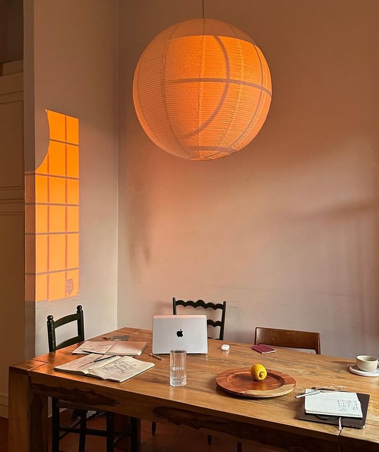 a wooden table topped with a laptop computer next to a yellow light hanging from the ceiling