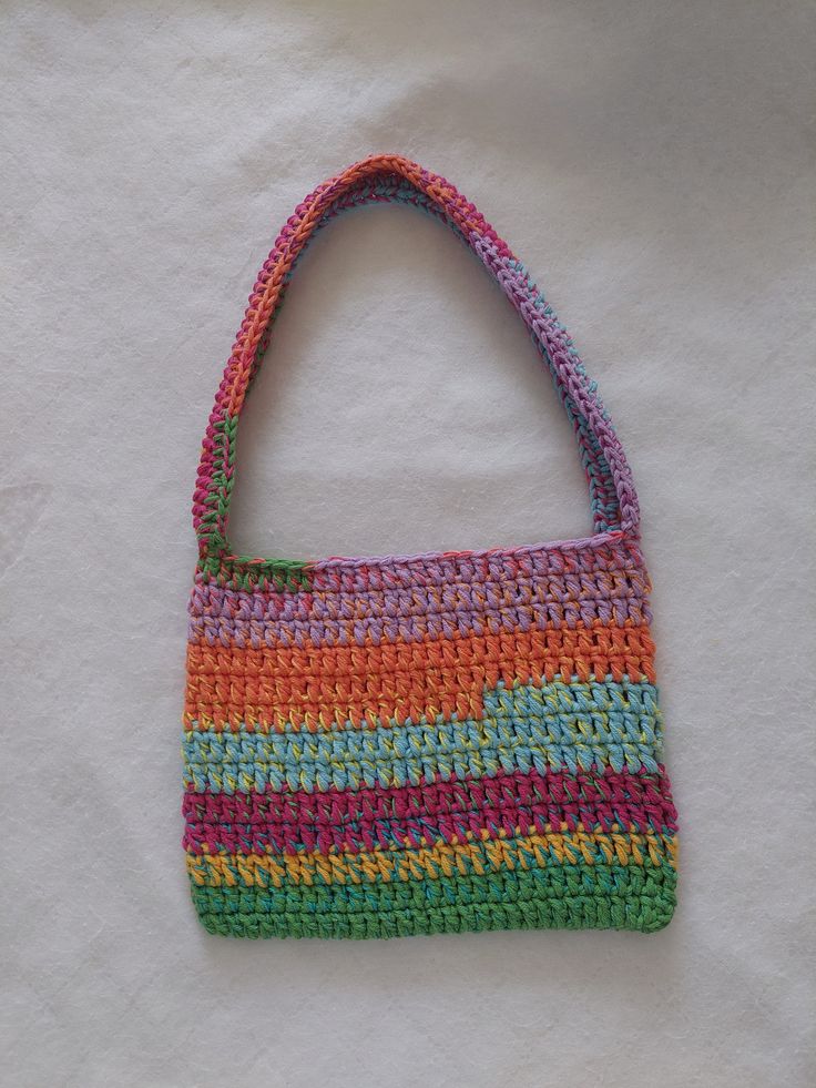 a multicolored crocheted purse sitting on top of a white sheet covered floor