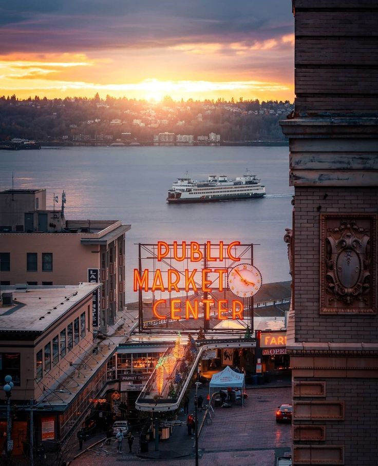 the public market center sign is lit up at sunset with boats in the water behind it