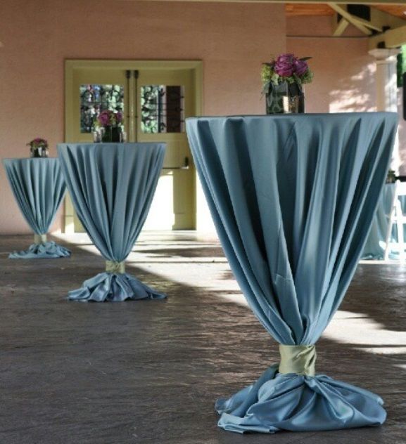 several tables with blue cloth draped over them and flowers in vases on the table