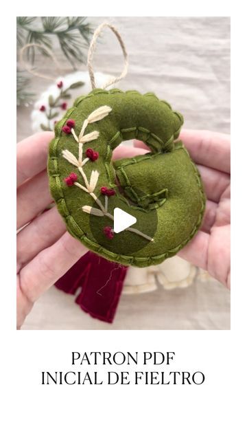 a hand holding a green felt ornament with leaves and berries on the front