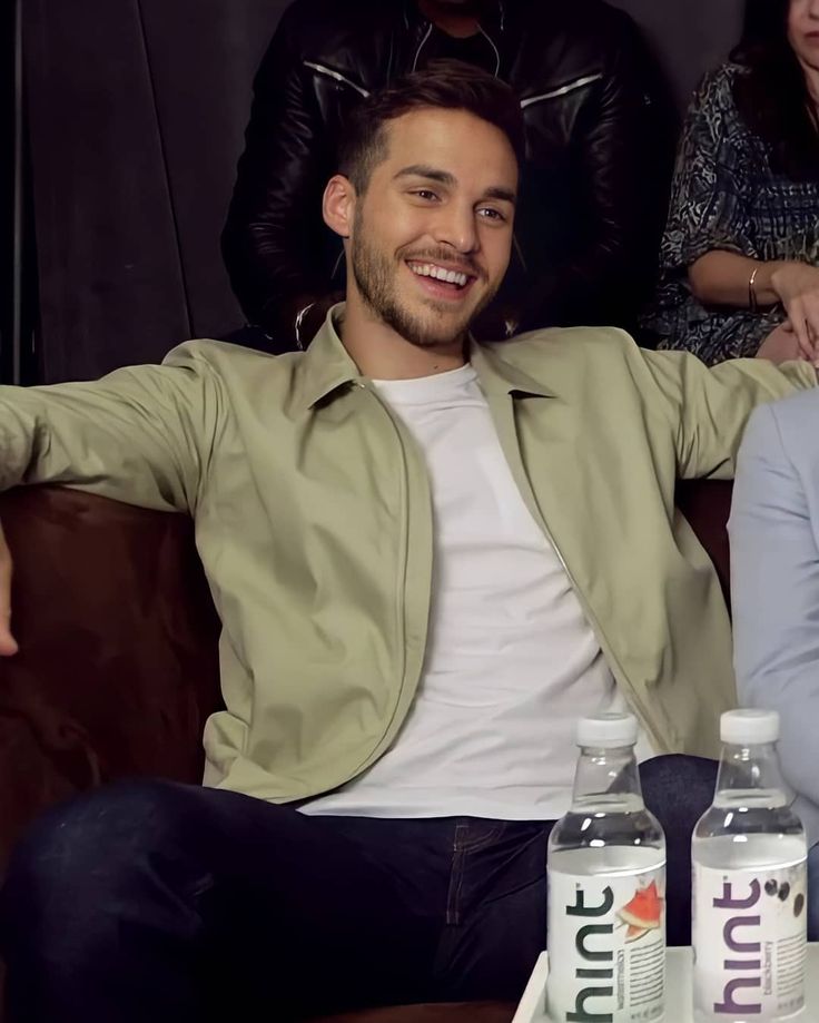 a man sitting on a couch next to two bottles of juice and a woman standing behind him