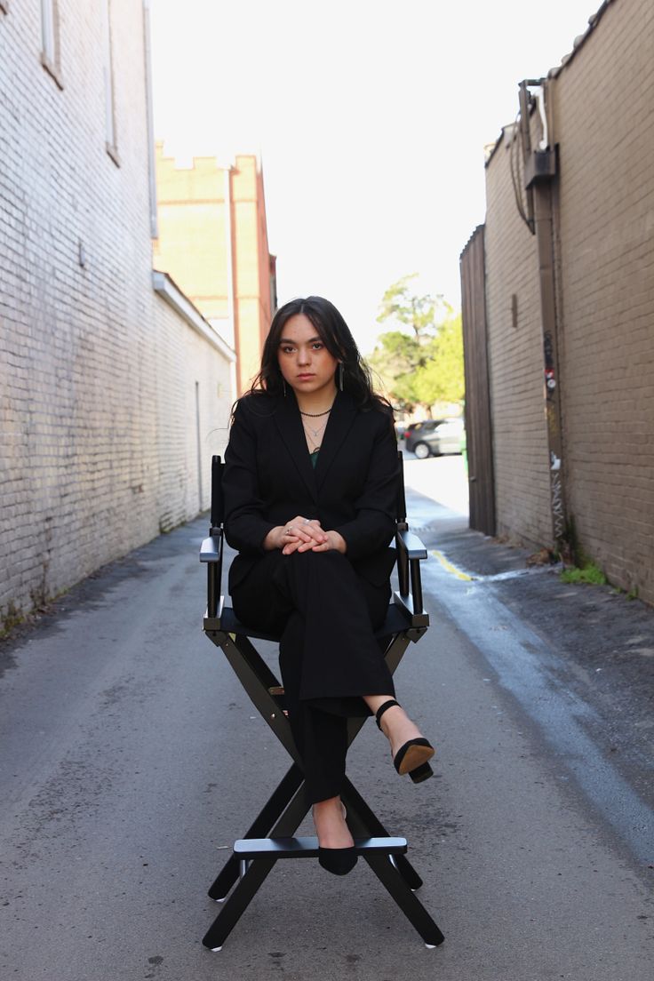 a woman sitting on top of a chair in the middle of an alley way with her legs crossed