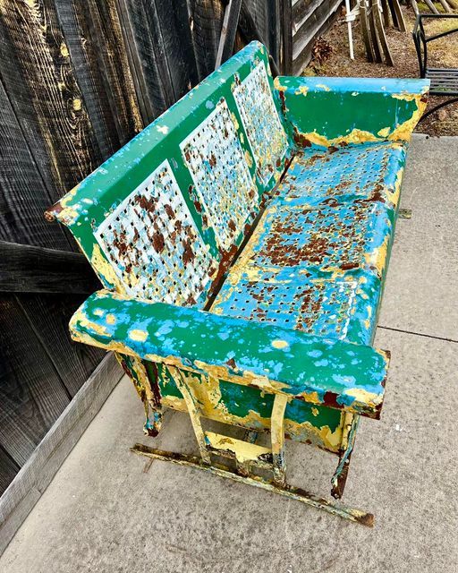 an old green and yellow bench sitting on the sidewalk