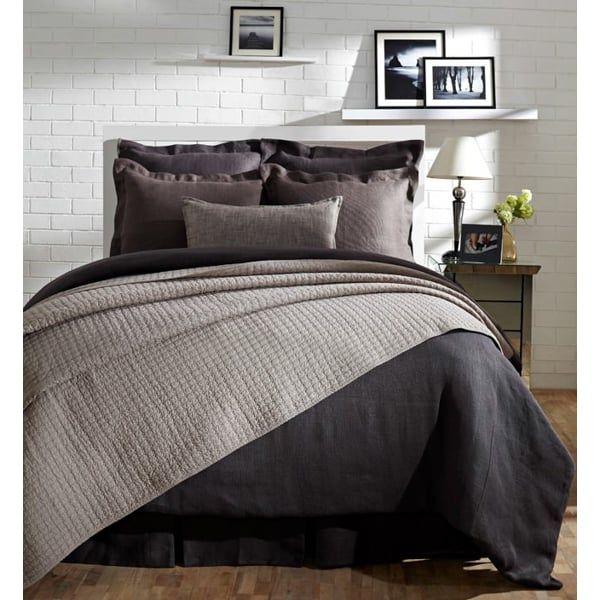 a bed with grey and black comforters in a white walled room next to pictures on the wall