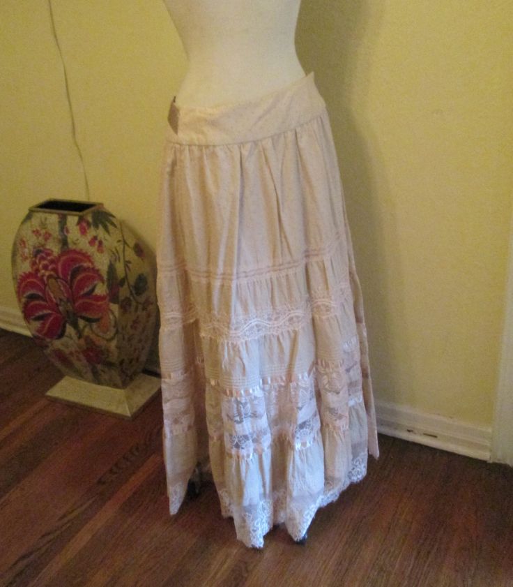 Vintage Bebe maxi skirt lace trim oatmeal color and gorgeous. This skirt is elegant with a boho style.  The waist is very flattering. It has inner buttons to wrap the skirt around. The skirt has wonderful embroidery with silk (or satin)ribbons and lace. You can tie the silk sash in the front, back or wrap around. It's made of a sturdy cotton and would look great with sandals or boots, can be worn with a tee shirt, a delicate blouse or short jacket (or any other way you think). Works for casual and dressy occasions. This skirt is suitable to be worn summer or winter. In excellent condition. It is marked small but please see measurements below, it could fit a medium poss a large. You also can move the buttons to tighten or loosen it. Measurements: Waist. 30" Hips. 42" full Length. 41" Thanks Feminine Cream Skirt With Lace Trim, Beige Lace Trim Skirt For Spring, Beige Skirt With Lace Trim For Spring, Beige Lace Long Skirt, Bohemian Tiered Skirt With Crochet Trim, Beige Cotton Skirt With Lace Trim, Beige Bottoms With Lace Trim Flowy Design, Feminine Beige Skirt With Lace Trim, Beige Long Skirt With Lace Trim