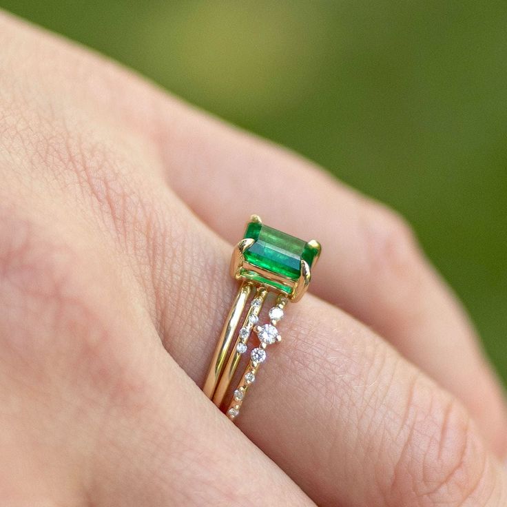 a close up of a person's hand holding an emerald and diamond ring