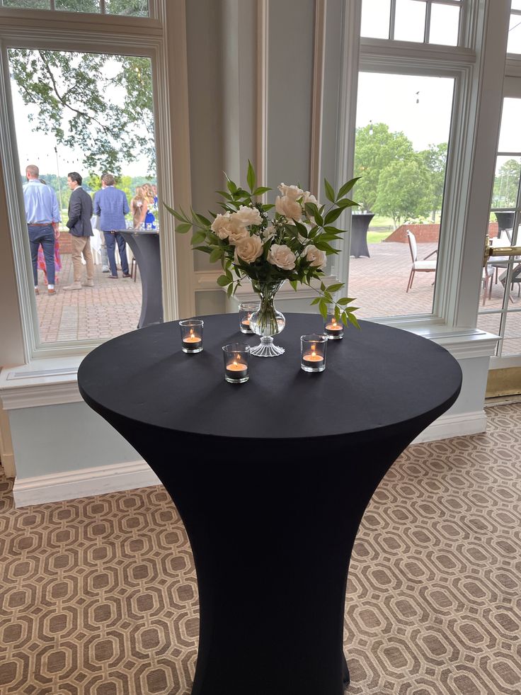 a table with candles and flowers on it in front of large windows at an event