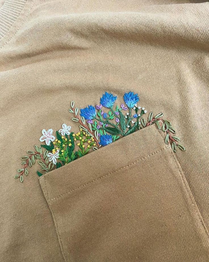 an embroidered pocket with flowers in it on a tan shirt that is rolled up to the side