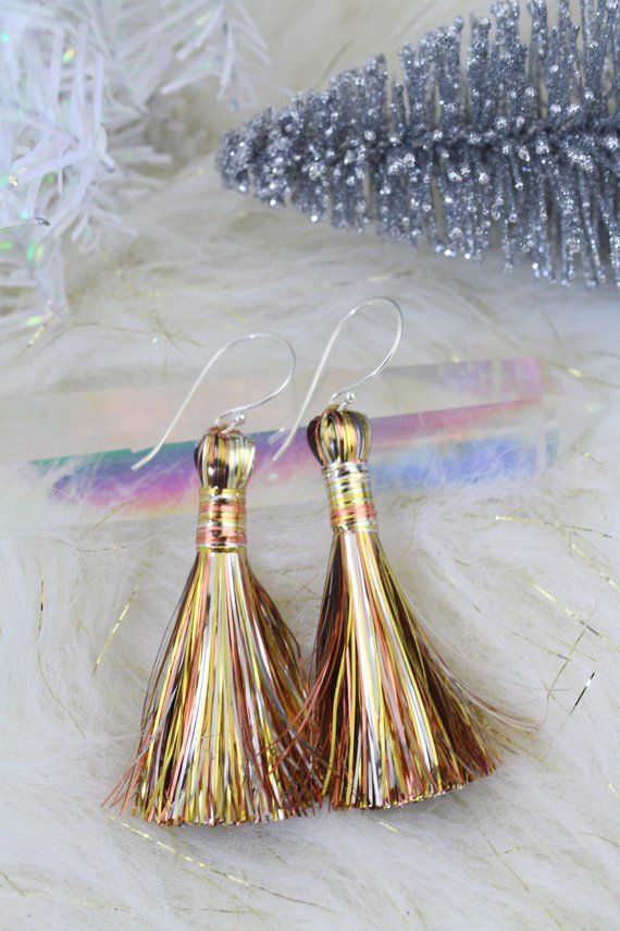 two gold tasseled earrings sitting on top of a white fur covered floor next to a christmas tree