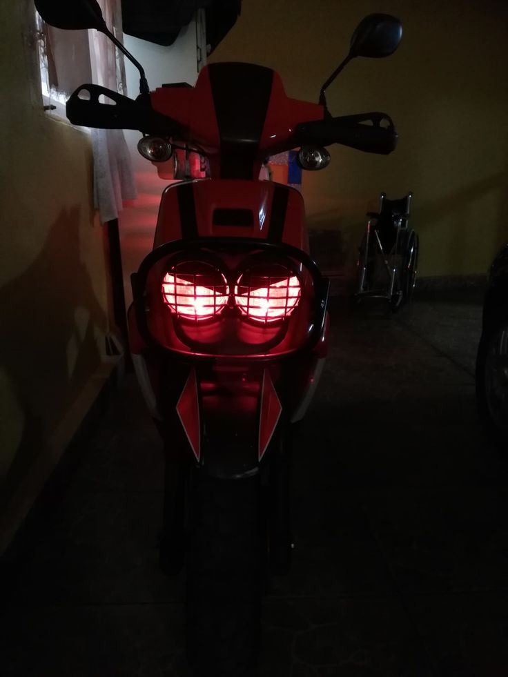 a red motorcycle is parked in the dark with its lights on and it's tail light turned off