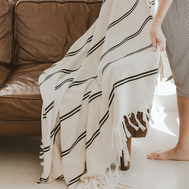 a woman standing next to a brown couch under a white and black striped throw blanket