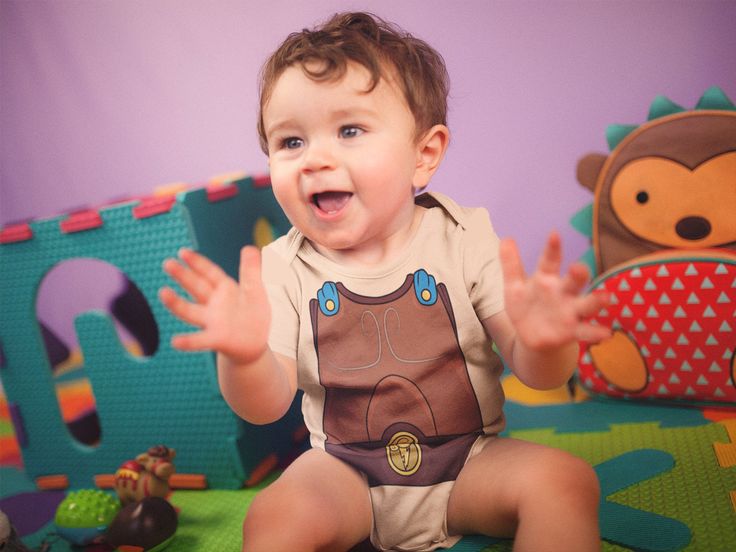 a toddler sitting on the floor with his hands in the air and smiling at the camera