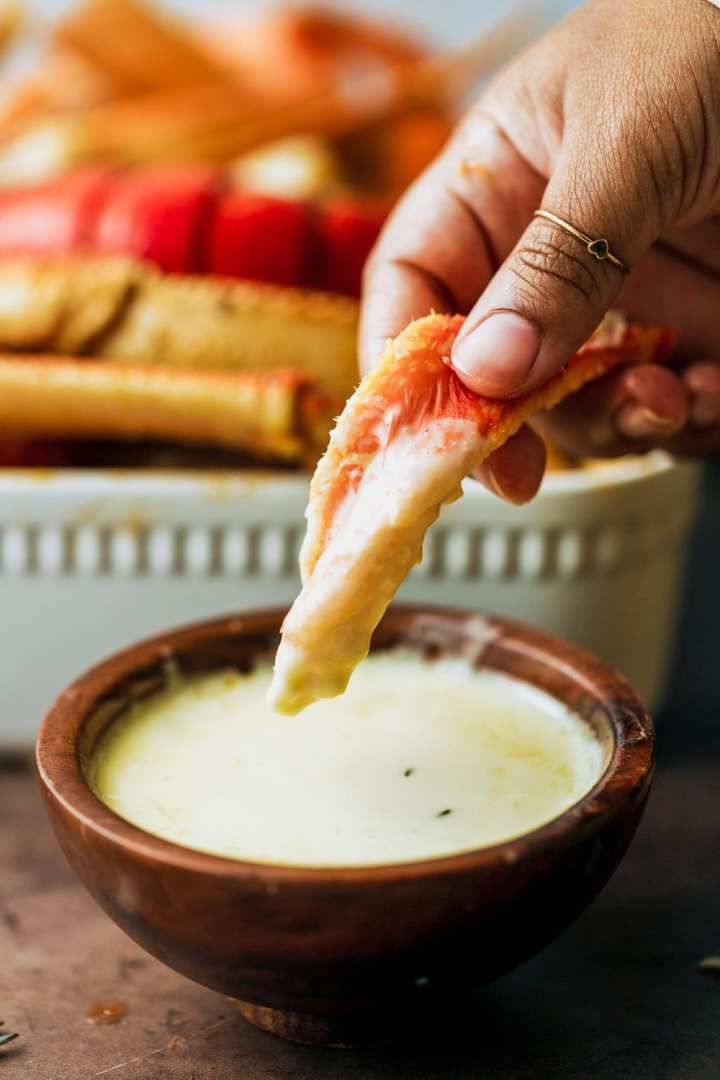 a person dipping sauce into a bowl with food on the table in the back ground