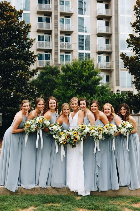 a group of women standing next to each other in front of a building with sunflowers