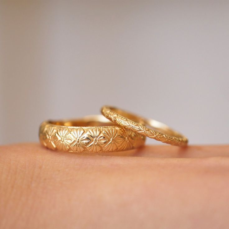 two gold wedding rings sitting on top of someone's arm with their fingers touching each other