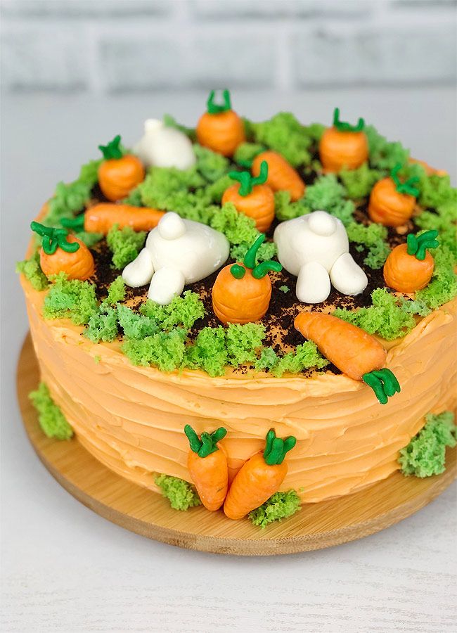 a cake decorated with carrots, broccoli and cauliflower on a wooden platter