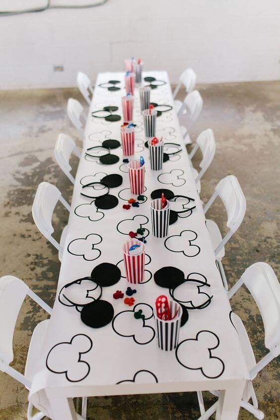 a long table is decorated with mickey mouse cups and popcorn buckets for an event