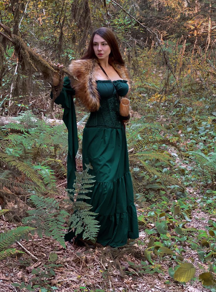 a woman in a green dress is standing in the woods with a fur stole around her neck