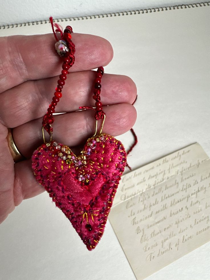 a hand holding a pink heart shaped beaded keychain with a note in the background