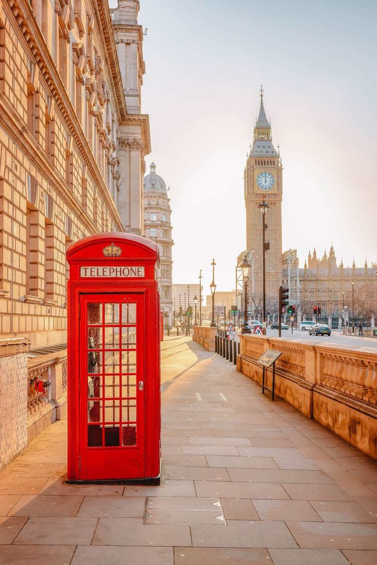 a red phone booth sitting on the side of a road next to a tall building