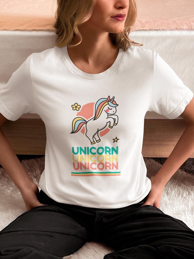 Unleash your magical side with our "Triple Unicorn Magic" t-shirt! This enchanting design features a beautifully illustrated unicorn above the word "unicorn" repeated three times for extra charm. Perfect for dreamers and fantasy lovers, this tee brings out the wonder and whimsy in anyone who wears it. Made from soft, premium fabric for ultimate comfort, it's a stylish and fun addition to your wardrobe. Whether you're a fan of unicorns or just love a touch of magic, this shirt is the perfect way to express your mythical style! Order and Shipping: * All our t-shirts are made to order, leveraging our order on demand printing partners * Please allow 1-3 days for production and 2-5 business days for standard shipping. Please reference expected shipping times for your location during checkout. P Fun Unicorn Print T-shirt For Summer, Fun Unicorn Print Short Sleeve T-shirt, Fun Short Sleeve T-shirt With Unicorn Print, Multicolor Cotton T-shirt With Unicorn Print, Multicolor Unicorn Print Crew Neck T-shirt, Summer Unicorn Print Short Sleeve T-shirt, Summer Short Sleeve Unicorn Print T-shirt, White Unicorn Print Crew Neck Top, Cute Rainbow Print Crew Neck T-shirt