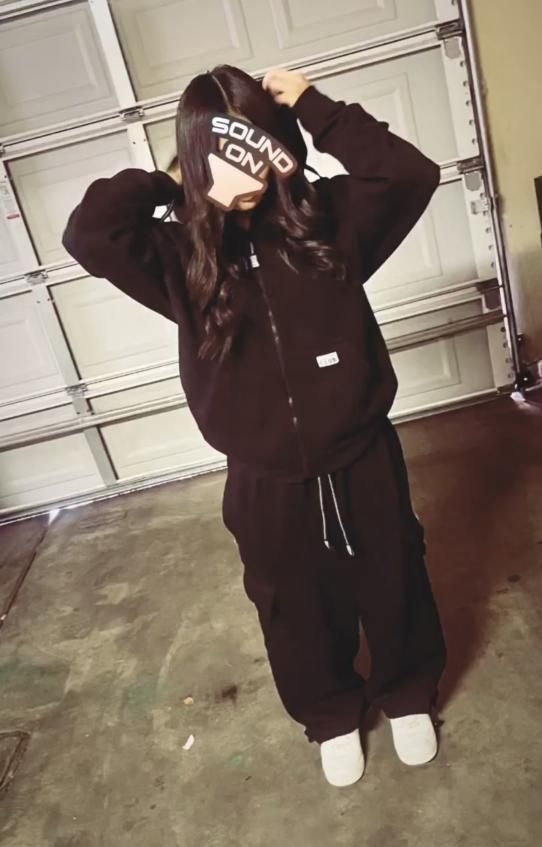 a woman standing in front of a garage door wearing a black sweatshirt and sweatpants