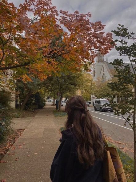 a woman is walking down the sidewalk with her back to the camera and looking at trees