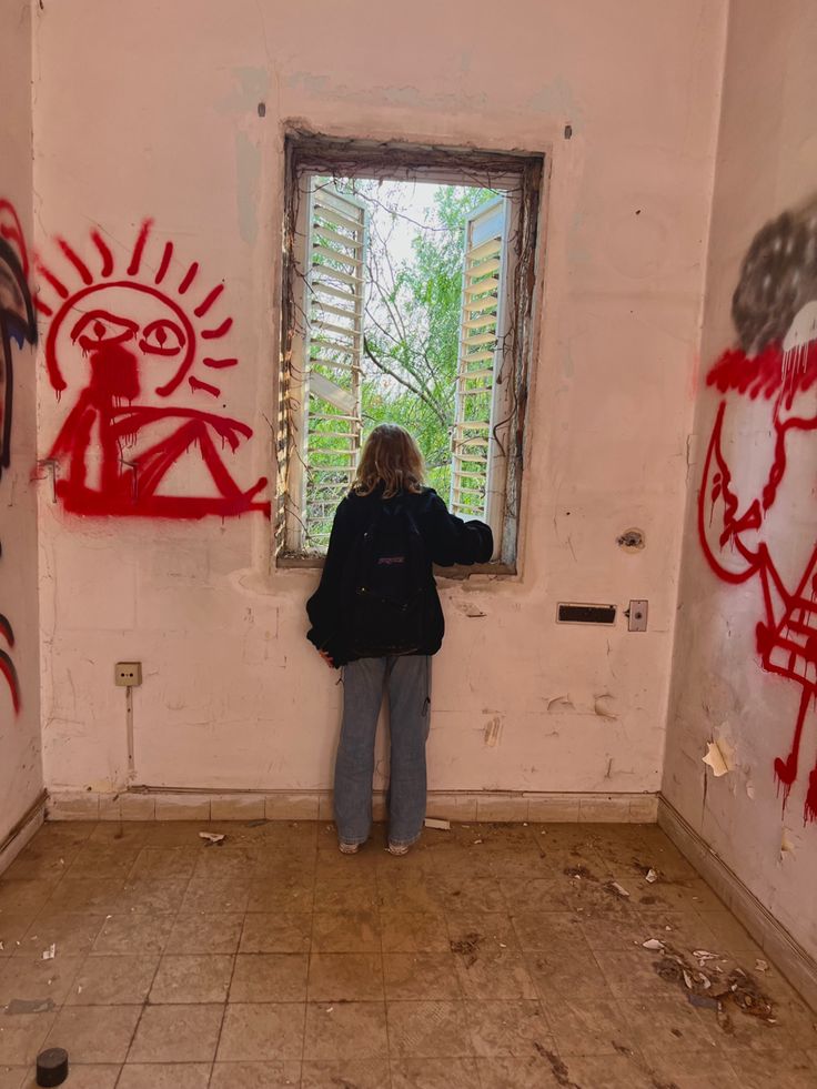 a woman standing in front of a window with graffiti on the walls and flooring