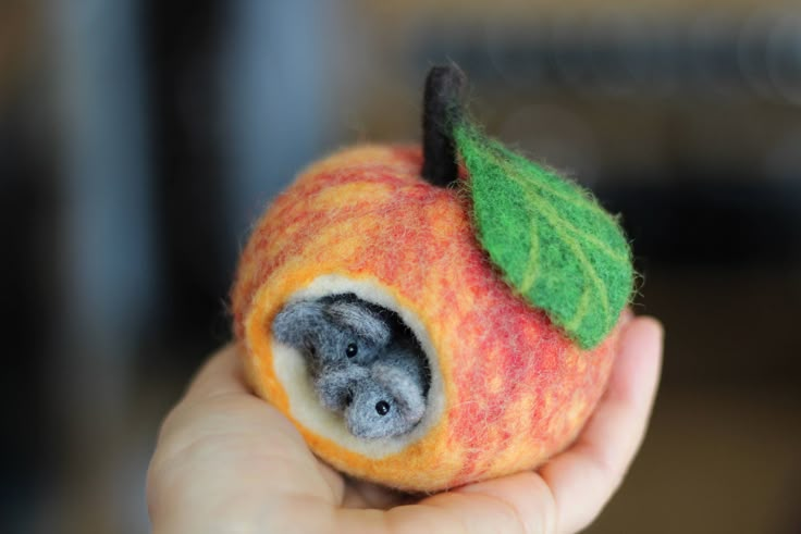 a hand holding an apple with a small animal in it's center and a green leaf on top